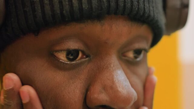 Closeup black man rubbing eyes, beanie headphones, latenight student and music producer, fatigue and stress, sweat on brow, reflective expression, yellow background, studio light, screen glow, moment
