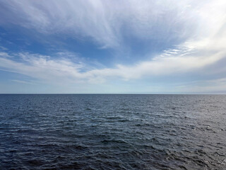 Fototapeta premium Open sea with calm blue water and sky clouds.