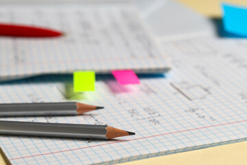 Naklejka premium Copybook with handwritten maths formulas with pencils on yellow background, closeup