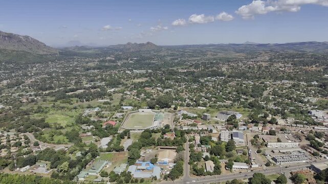 Drone facing southwest, flies to the right with entirety of city below on a sunny day in Zomba, Malawi