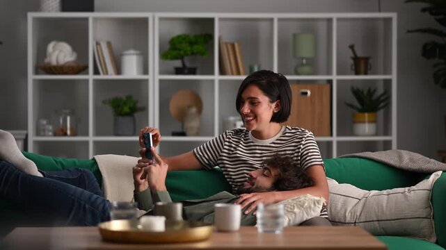 Happy young couple laughing and taking selfies together on the couch at home in the living room