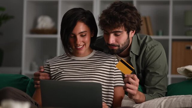 Couple enjoying online shopping with credit card and laptop at home while ordering goods from the couch at night