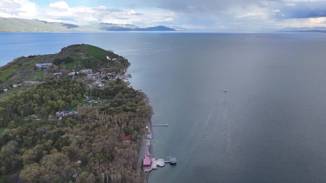 4K Drone Aerial View of Mountain Lake Shoreline With Floating Boat Under Dramatic Cloudy Sky.