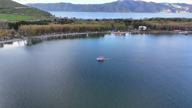 4K Drone Aerial View of Mountain Lake Shoreline With Floating Boat Under Dramatic Cloudy Sky.