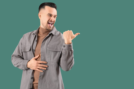 Young man laughing at something on green background. Accusation concept