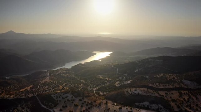 Panoramic landscape of Troodos mountains and an artificial reservoir during golden hour sunset, with the Mediterranean Sea visible on the horizon. Travel Cyprus rural nature. Aerial view drone flight