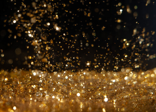 Gold dust floats in the air with light reflecting at a dark location