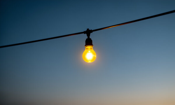 A Single Glowing Edison Light Bulb Hanging on a Wire Against Twilight Blue Sky