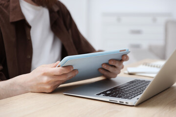 Fototapeta premium Man working with tablet at wooden table indoors, closeup