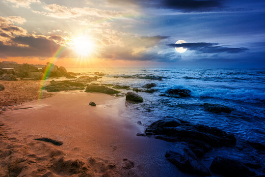huge stones on a sandy beach. day meet night. epic summer vacation season at the black sea. sun and moon in harmony over calm waves washing the sand shore. nature background with cloudy sky