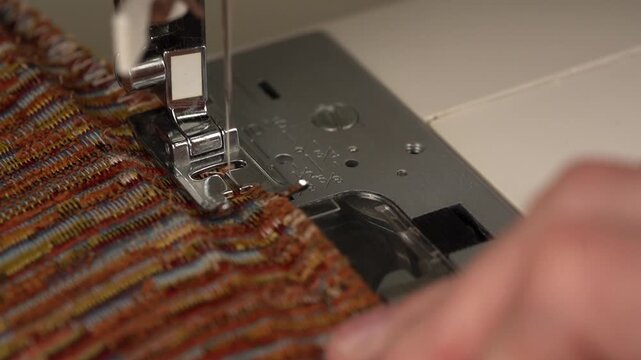 Close-up of seamstress hands guiding fabric under a sewing machine needle creating a decorative overlock imitation zigzag stitch for edge finishing.