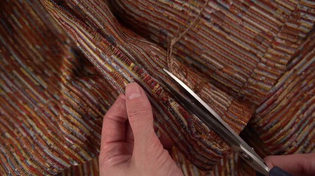 Wider close-up of hands using scissors to trim loose threads sticking out from woven fabric after sewing.