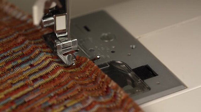 Close-up of a sewing machine needle and presser foot sewing a decorative zigzag overlock imitation stitch on fabric edge.