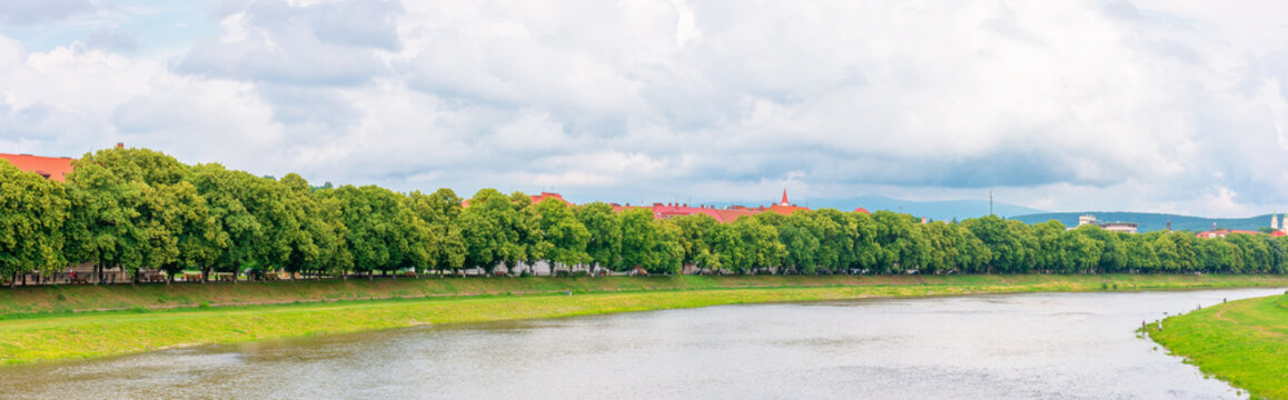 longest linden alley in europe on the Uzh river embankment. lime trees on a sunny summer afternoon. travel destination of transcarpathia. uzhhorod street cityscape beauty. panorama