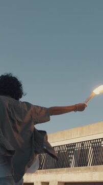 A skateboarder, embodying the spirit of adolescence, performs a daring trick on a rooftop, arms outstretched with torches in each hand, their flames casting a warm glow against the twilight sky.