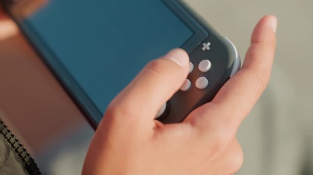 Closeup hands holding handheld console during fast gameplay, thumb pressing buttons and triggers, quick finger reactions, tense competitive energy, focus on touchscreen and input, youthful player