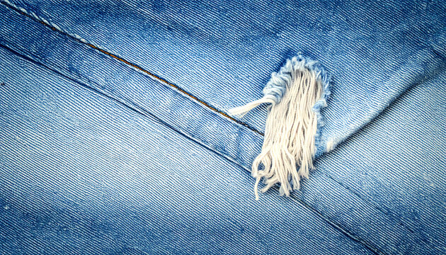Close up of ripped blue denim fabric texture with visible threads and weave, distressed jeans material