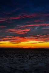Fototapeta premium Vibrant sunset over a vast landscape with dramatic orange and purple clouds.