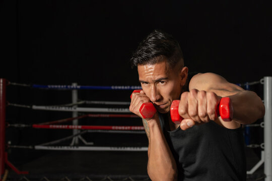 young Hispanic boxer throwing weighted punch with dumbbells in gym