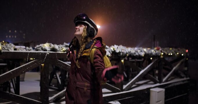 Happy Snowboarder Girl Dancing in Falling Snow at Night Ski Resort