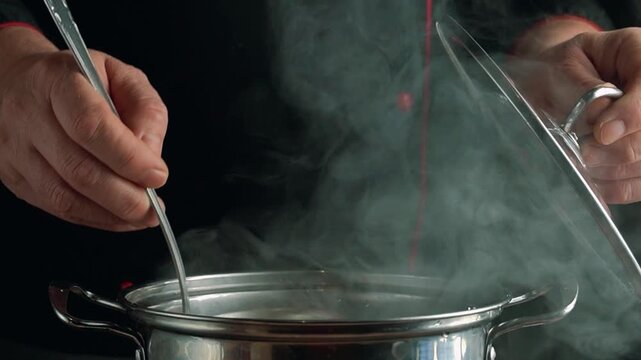The chef removes the lid from the pot, allowing steam to escape, stirring the buckwheat with a ladle, demonstrating the cooking process in a well-lit kitchen environment