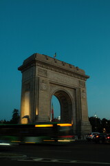 Fototapeta premium A city in motion at blue hour, with light trails and traffic flowing past Bucharest’s Arcul de Triumf.