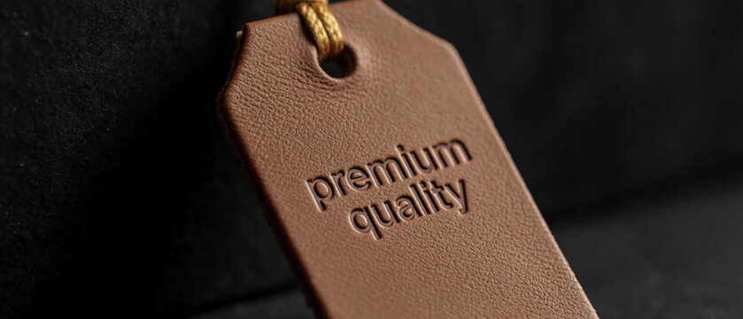 Brown leather tag with "premium quality" debossed, gold string, dark backdrop.