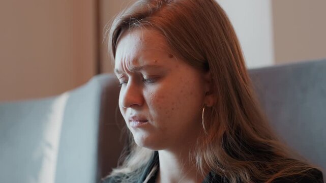 Young woman inspecting salad, face shows disgust and hesitation while seated in cafe, fork and knife poised over bowl of greens, close portrait captures contemplative conflicted mood and soft natural