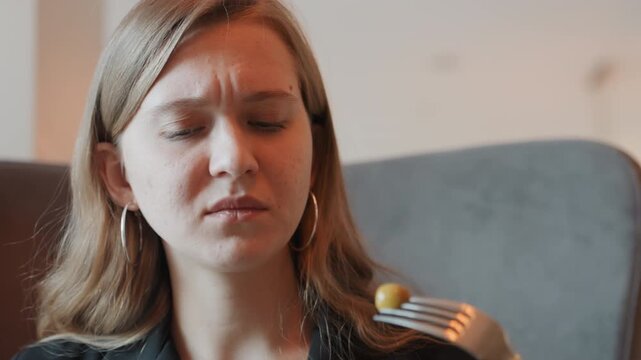 Caucasian woman reacts to olive on fork, student turned food critic expression, furrowed brow and subtle grimace, tasting hesitation, hoop earring detail, closeup portrait with soft indoor light,