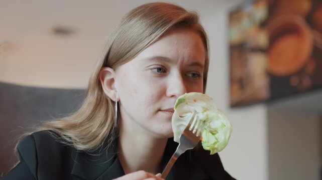 Woman tasting crisp lettuce in cafe, slow mindful bite, fork closeup, gentle smile of satisfaction, warm daylight, modern interior with menu board background, health blogger vibe, fresh organic