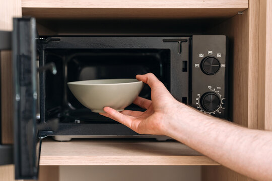 Man is heating lunch, put bowl in kitchen microwave