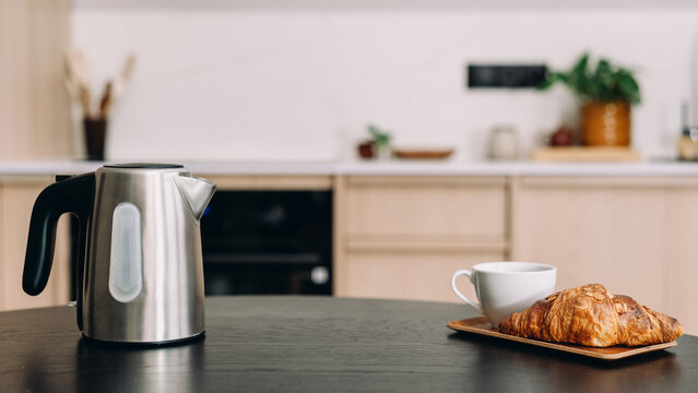 Stainless steel electric kettle and croissant on kitchen table