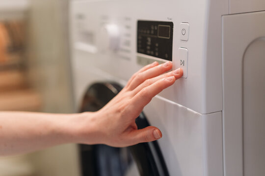 Woman pressing start button on modern laundry machine