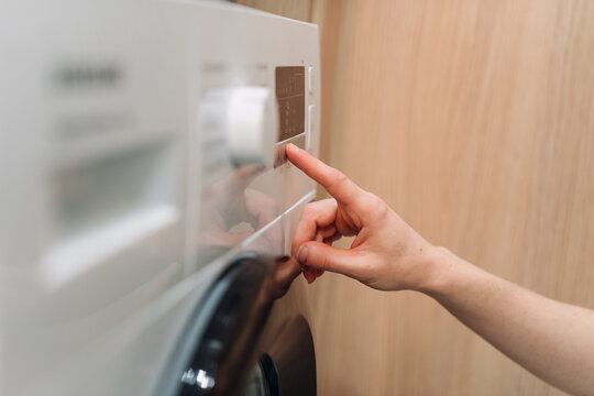 Woman press start button on modern automatic washing machine