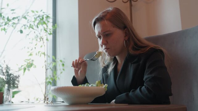 Lady reacts poorly to food. Woman exhibits disapproval after trying unappealing lunch bite. Lady grimaces and expresses discontent upon sampling unappetizing salad during her work break