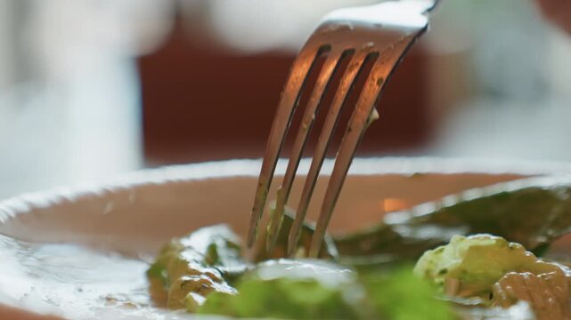 Closeup fork piercing romaine lettuce on white plate, cozy restaurant setting, fork tines pressing crisp basil leaves with creamy dressing, warm bokeh background, slow cinematic motion capturing