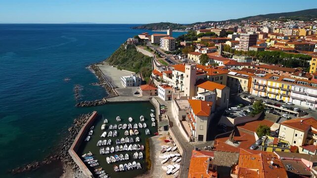 Piombino Tuscany Aerial 4K. Drone cinematic flyover over fishing boat marina making turn to reveal old town cityscape and famous lighthouse landmark. Scenic Tuscany maritime coast landscape
