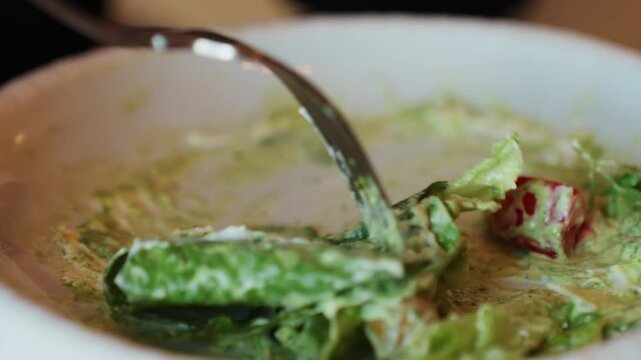 Fork lifting creamy romaine lettuce bite, closeup of dressed salad in white bowl with cherry tomato and croutons, glossy dressing coating leaves, messy smear on plate, intimate restaurant mood,