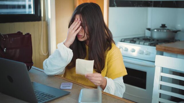 Video of a young Caucasian woman doing calculations with her calculator and feeling sad because she cannot pay her debts. Concept of economic and financial problems.
