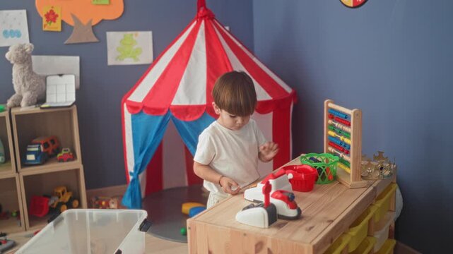 Boy presses buttons on a toy cash register and touches abacus beads inside a play tent studio; concentration.