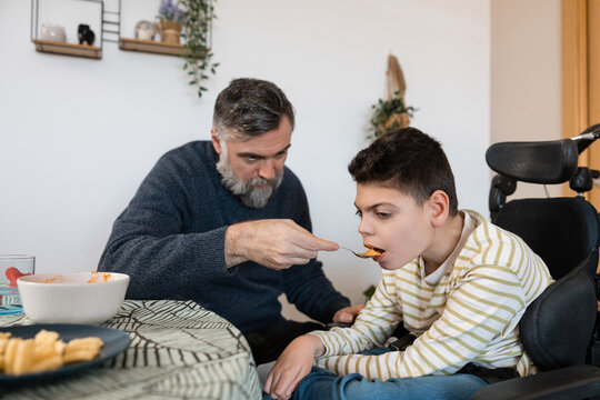 Father feeding son with cerebral palsy in wheelchair