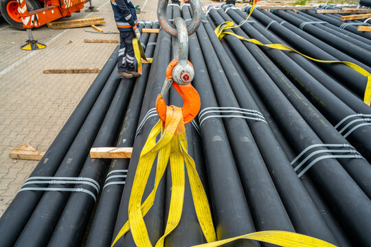 Industrial lifting hook and heavy duty slings on stacked steel pipes at logistics yard, cargo handling and construction industry transportation concept