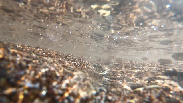 An underwater view of a shallow, clear stream. Small fish swimming over a sandy, gravelly bottom and movement on the water&rsquo;s surface. Stock footage of nature and a stream ecosystem.