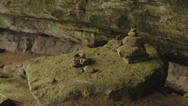 Small, hand-stacked stone cairns perched on a mossy boulder inside a rock shelter.
