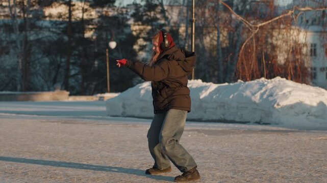White woman on frozen parking lot leaning backward while arms flail, red gloves, thick coat, boots digging into ice, moment of shock turning into cautious grin, urban winter scene