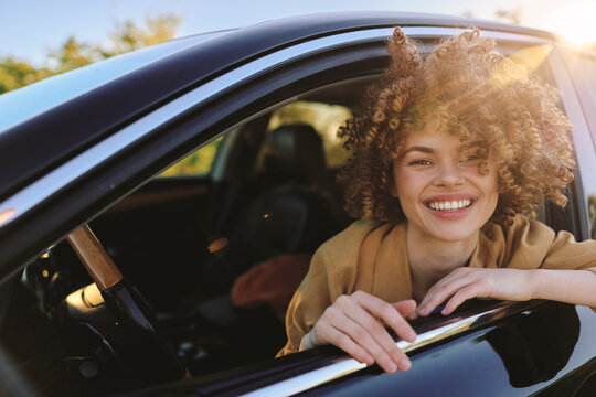 A smiling woman leans from a car window, enjoying sunny outdoor vibe with retro film color and warm light, celebrating casual lifestyle and free road trip moments.
