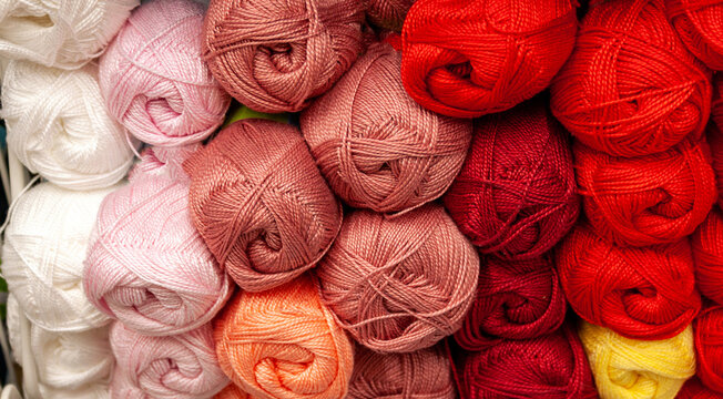 Colorful balls of yarn in different shades of red, white, pink, peach, and yellow stacked in rows.