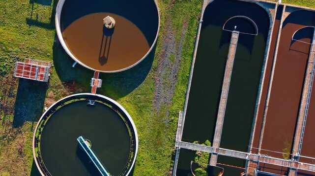 Aerial top down view of water clarification tanks facility. Overhead drone shot of circular and rectangular clarifier tanks in a modern sewage treatment processing facility.