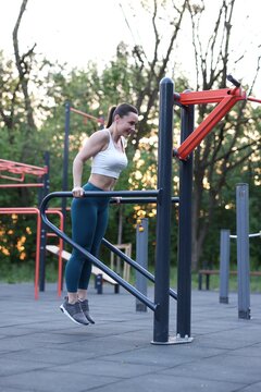 Athletic woman exercising on parallel bars at outdoor gym