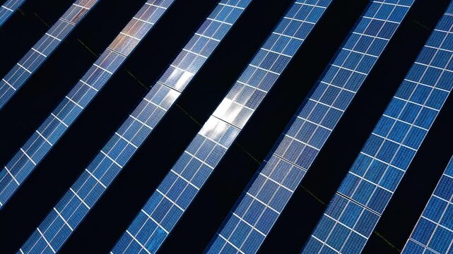 Diagonal pattern of solar panels array close up view. Abstract top-down aerial close up of solar panels arranged in tight diagonal rows with bright solar reflection.